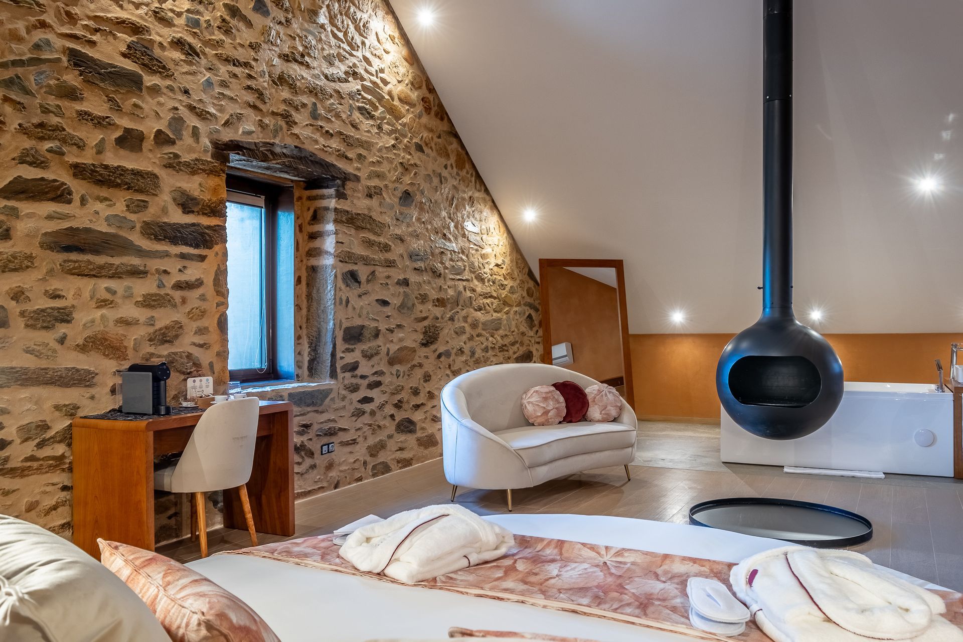 Suíte do hotel Cherry Covilhã, com paredes de pedra e lareira suspensa.